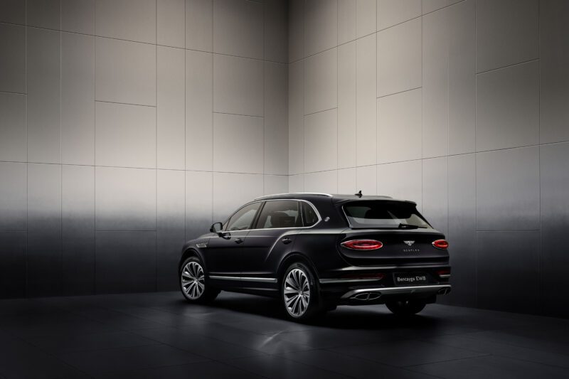 A black luxury SUV is parked in a dimly lit, modern showroom. The vehicle is positioned with its rear and side visible, showcasing sleek design features.