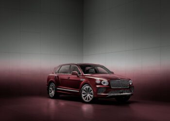 A maroon luxury SUV is parked in a minimalist, gradient-colored room with a reflective floor.