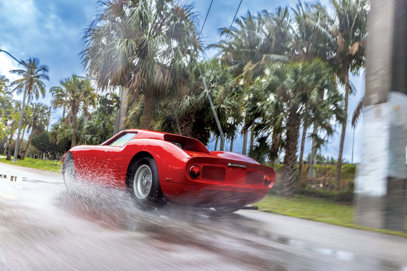 A red Ferrari 250 LM speeds swiftly along a wet road, palm trees swaying in the background, capturing the essence of a Cavallino Classic moment.