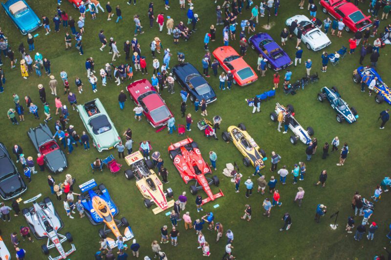 Pandangan udara menangkap pameran mobil yang ramai di Pulau Amelia, di mana mobil-mobil vintage dan balap menghiasi medan hijau, dikelilingi oleh kerumunan yang hidup di dekat Ritz-Carlton yang elegan.