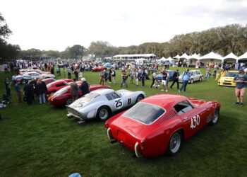 Set against the lush backdrop of the 30th Year celebration at the Ritz-Carlton, a car show featuring a stunning array of classic cars captivates attendees, with gleaming vehicles displayed on grassy expanses and white canopy tents dotted in the background.