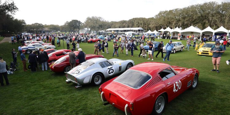 Set against the lush backdrop of the 30th Year celebration at the Ritz-Carlton, a car show featuring a stunning array of classic cars captivates attendees, with gleaming vehicles displayed on grassy expanses and white canopy tents dotted in the background.