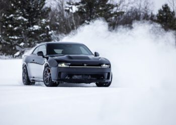 A black AWD muscle car slices through the swirling snow on a secluded road, with trees standing majestically in the background. This Dodge Charger proves its resilience as it tackles the wintry elements with ease.