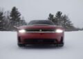 A red Dodge Charger with headlights piercing through the snowy landscape, gracefully navigating the path as an AWD muscle car, with trees standing tall in the background.