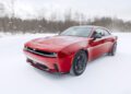 A red Dodge Charger, the AWD muscle car, navigates a snowy road with ease, its vibrant hue contrasting against the blurred forest background.