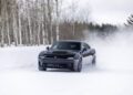 A black Dodge Charger, the world's only AWD muscle car, drifts through snow on a road lined with leafless trees.