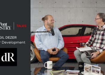 Two men are seated in a room with microphones, a red car in the background, and materials on a glass table. The screen reads "duPont Registry Talks," featuring Gil Dezer from Dezer Development, delving into the world of luxury real estate and automotive living.