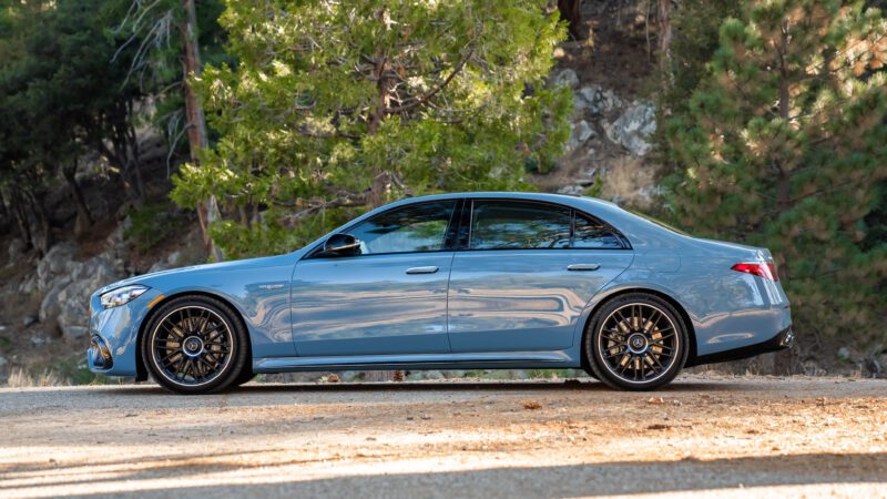 A Mercedes-AMG S63 sedan parked on a dirt road with a background of trees and rocks.