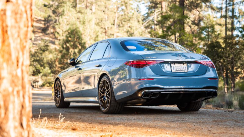 A blue sedan parked on a dirt path in a forested area with trees in the background.