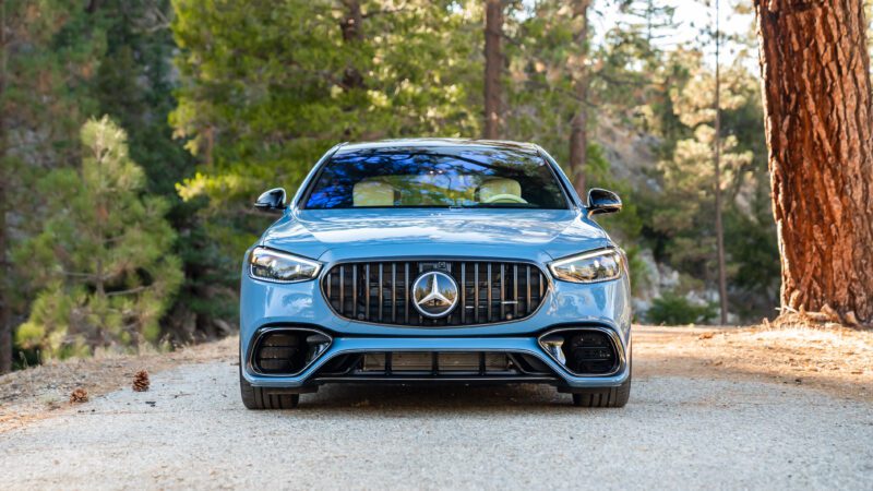 Front view of a blue Mercedes-AMG S63 parked on a forest road, surrounded by trees.