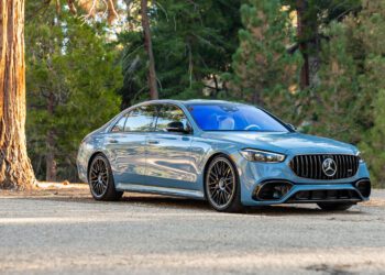 A blue luxury sedan parked on a forest road with tall trees in the background.