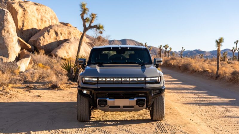 A black off-road vehicle on a desert dirt road, surrounded by rocks and Joshua trees under a clear blue sky.