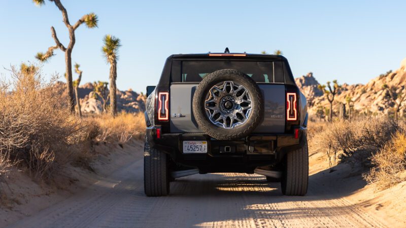 A rugged SUV with a spare tire mounted on the back drives down a sandy desert road lined with Joshua trees.