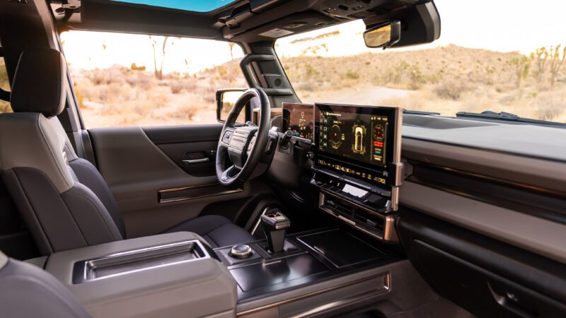 Interior of a modern vehicle featuring a steering wheel, digital dashboard, and touchscreen display, with desert scenery visible through the windows.