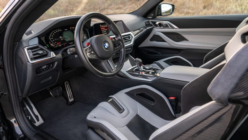 Interior of a BMW car, featuring a steering wheel, digital dashboard, gearshift, and bucket seats with a mix of gray and black upholstery.