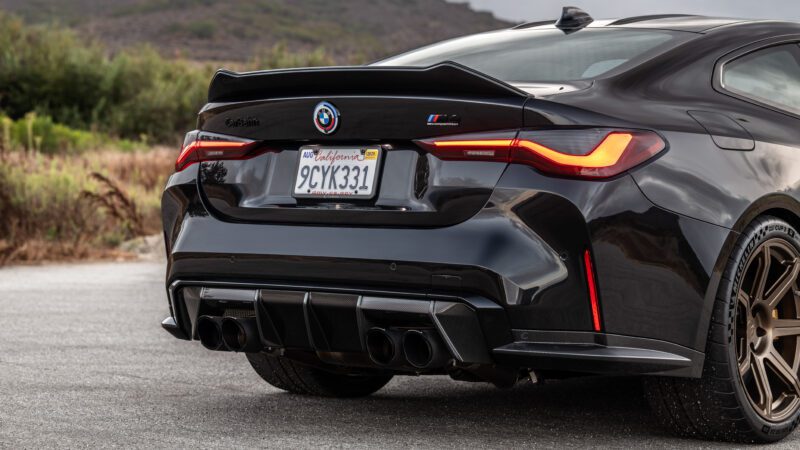 Rear view of a dark gray sports car parked on a road, showing dual exhausts, aerodynamic detailing, and a California license plate.