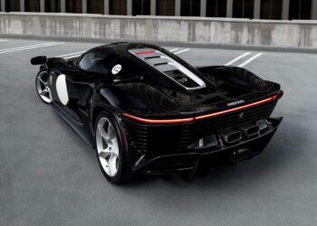 A sleek, black Ferrari Daytona SP3 sports car is parked on a Beverly Hills rooftop with a modern building in the background. The car boasts a low profile, aerodynamic design, and distinctive rear lights.
