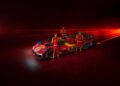 Three individuals in red racing suits stand beside a stunning red Ferrari race car, its 2025 livery shimmering with racing decals against a dimly lit background infused with red accents.