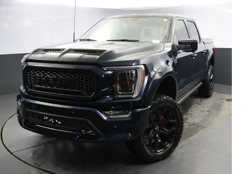 A unique creation, this black pickup truck with off-road tires stands proudly in the showroom, facing three-quarters view.