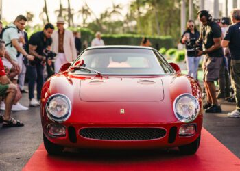 A red vintage Ferrari 250 LM sports car, often hailed as the Best of the Best, is parked on a red carpet, surrounded by a crowd of people snapping photos at the prestigious Cavallino Classic event.