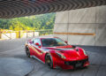 A red sports car is parked on a modern driveway, set against the scenic backdrop of green hills and the exclusive Magarigawa Club.