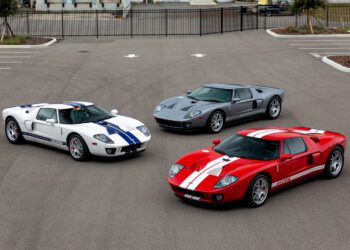 Three iconic Ford GT cars, including a rare 2006 model, are parked side by side: one white with blue stripes, one sleek grey, and a striking red with white stripes. These beauties make any car enthusiast eager to win the bid for such vintage treasures.