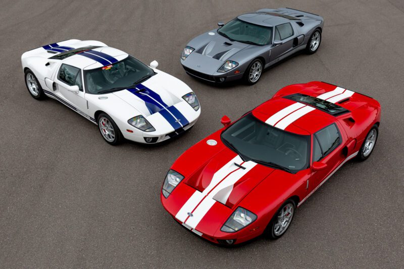 Tiga Ford GT 2006 diparkir di permukaan beraspal, menampilkan warna -warna mencolok mereka: putih dengan garis -garis biru, abu -abu dengan garis -garis putih, dan merah dengan garis -garis putih. Dilihat dari sudut tinggi, keindahan ini mungkin hanya membuat Anda ingin memenangkan tawaran.