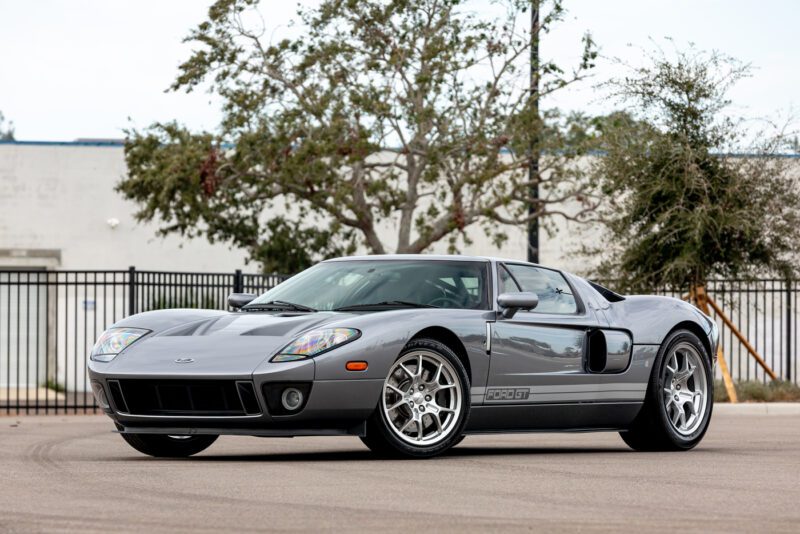 Mobil sport Ford GT 2006 yang ramping, dicat dengan abu -abu yang mencolok, terletak dengan elegan di trotoar. Dengan pohon -pohon yang bergoyang dengan lembut dan pagar berdiri tegak di belakangnya, model indah ini mengundang Anda untuk memenangkan tawaran dan memiliki sepotong legenda otomotif.