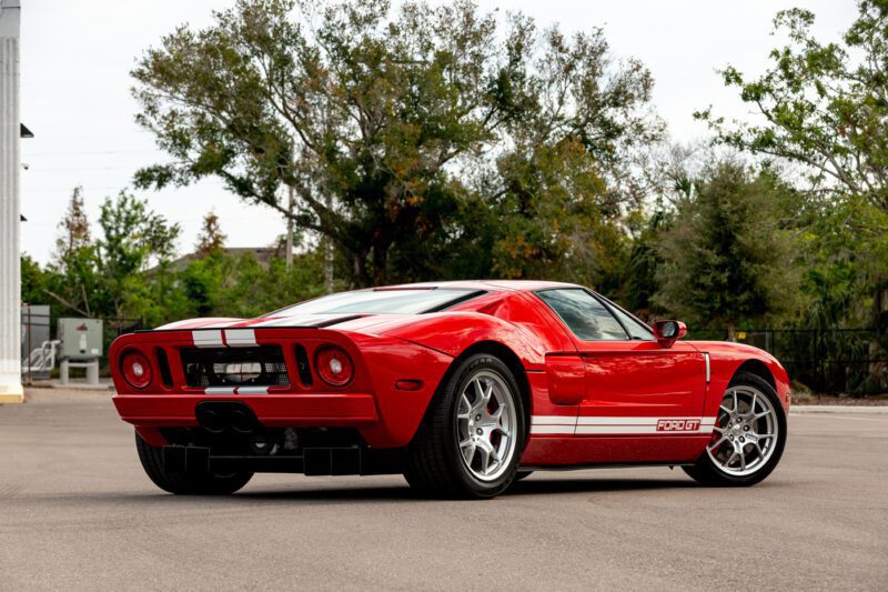 Mobil sport Ford GT 2006 merah berkilau di bawah matahari, diparkir di jalan yang tenang dengan pohon -pohon yang melapisi latar belakang. Ini adalah visi kekuatan dan keanggunan yang menunggu untuk memenangkan upaya setiap penggemar.