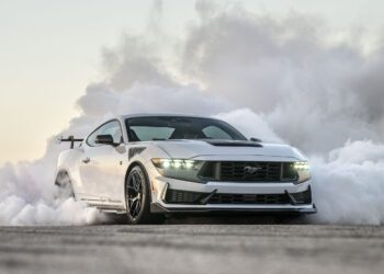 Sports car performing a burnout, surrounded by smoke, on a clear day.