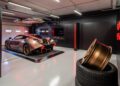 A sleek Hispano Suiza sports car is parked indoors with red accent lighting, evoking the allure of Circuit de Barcelona-Catalunya. Nearby, stacked tires and rims sit ready for action, reminiscent of the hustle at a trackside box.
