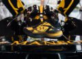 A black and yellow sports shoe is displayed on the rear wing of a sleek black car in a bright indoor space.