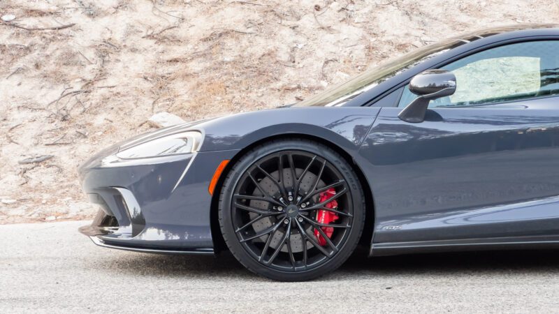 Close-up of a gray sports car with black rims and red brake calipers parked on a road.