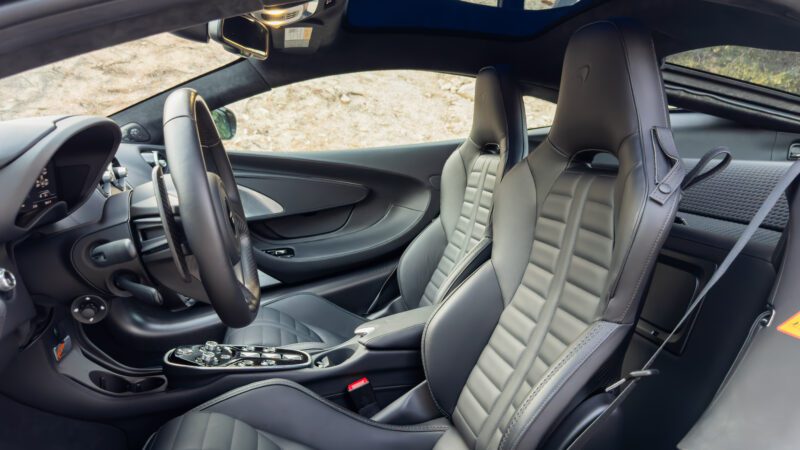 Interior view of a sports car showcasing two gray leather bucket seats, a sleek dashboard with a steering wheel, and a control console in the center.