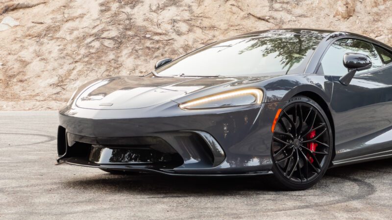 A gray sports car with red brake calipers is parked on a road with a rocky background.