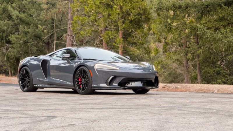 A gray sports car parked on a road with trees in the background.