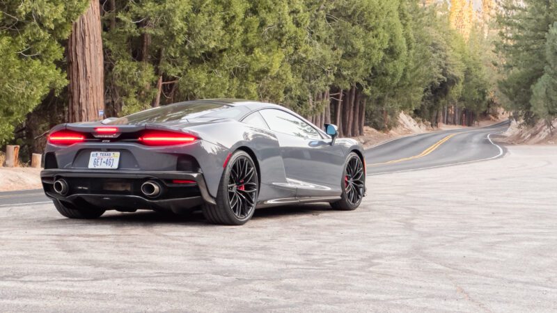 A sleek, gray sports car is parked on a scenic, winding road surrounded by tall trees.