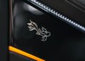 Close-up of a stylized dragon emblem on a glossy black surface, bordered by leather and an orange trim, reminiscent of the Mulliner Bespoke Collections.