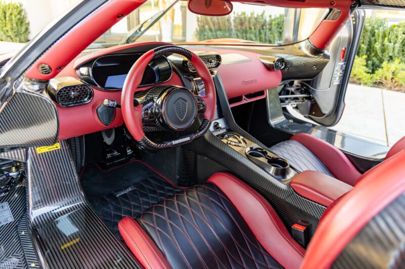 The interior of the extreme luxury sports car showcases a carbon fiber dashboard, red and black leather seats, and a prominently displayed steering wheel with detailed control buttons, reminiscent of the Koenigsegg Regeras.