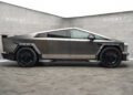 A futuristic, metallic gray Custom Tesla Cybertruck with an angular design and sleek elongation is parked indoors. The backdrop prominently features "Mansory" branding on the walls.