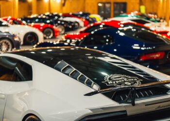 A row of exotic luxury sports cars, including a white car in the foreground with a HyperCars decal, is displayed indoors under warm lighting, offering an unparalleled buying experience.