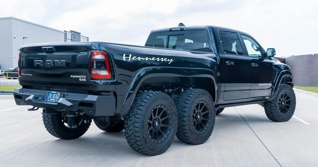 A large black six-wheel pickup truck with Hennessey branding on the side and rear is parked outdoors on a concrete surface. This impressive machine stands out among off-road exotics, making it a prime choice for those seeking unique performance vehicles.