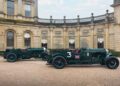 Two vintage Bentley green cars, part of the Continuation Series, bearing the number 3 and a British flag, are parked on a gravel driveway in front of an ornate building.