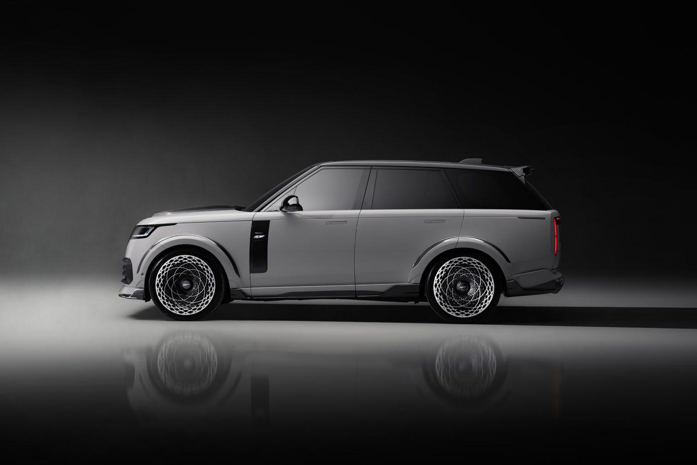 A sleek gray SUV, boasting the Overfinch Velocity Edition, features tinted windows and intricate alloy wheels. Displayed against a dark gradient background, its powerful aesthetic gleams in the reflection on the floor beneath.