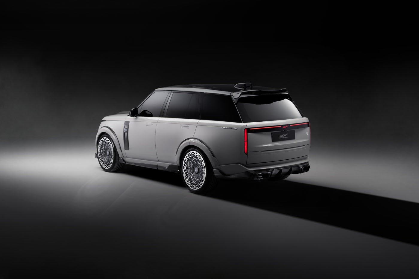 A sleek, modern SUV in a dimly lit space, showcasing its rear and side profile with a metallic gray finish and intricate wheel design, embodies a powerful aesthetic reminiscent of the Overfinch Velocity Edition.