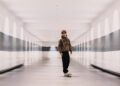 A skateboarder glides effortlessly through the sleek, modern corridor of McLaren Headquarters, where white walls and reflective surfaces echo the elegance of an Artura Spider.