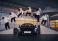 A skateboarder in a white jacket performs a sequence of tricks, captured in multiple frames, over a sleek black McLaren Artura indoors.