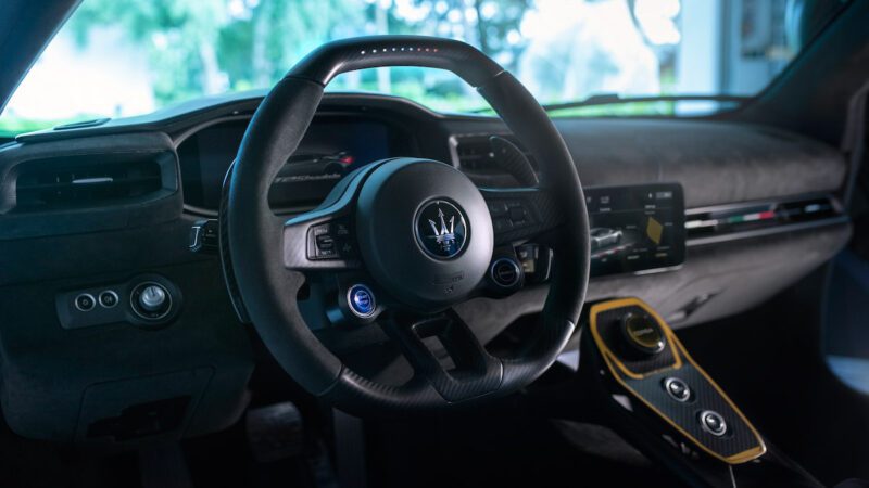 Interior view of a car showcasing the steering wheel with a trident logo, dashboard with digital displays, and modern controls in a sleek design.