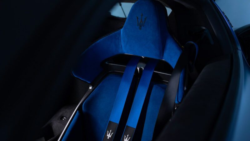 Close-up of a blue car seat with four-point seatbelts featuring a trident logo.