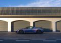 A sleek blue Maserati GT2 Stradale is parked in front of a modern building with three closed gray garage doors and a striped upper facade, capturing the essence of luxury in a picturesque corner of Spain.